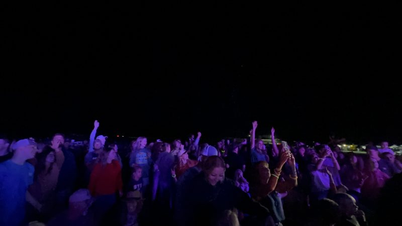 A wide nighttime crowd of SodFest attendees facing the stage with arms raised, kids visible in the front rows and venue lights twinkling along the back horizon.
