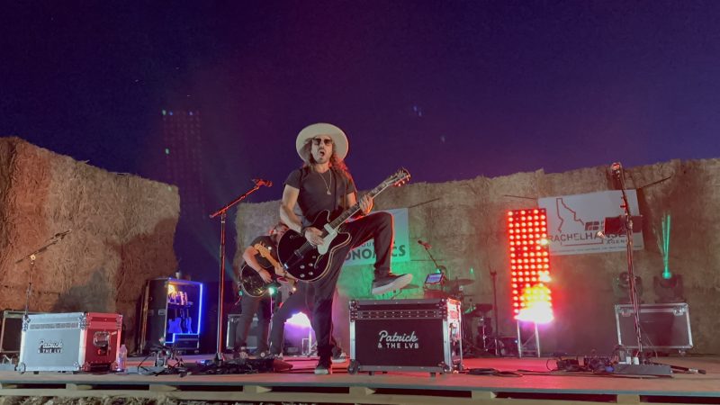 Patrick & the LVB on the hay-bale stage with the frontman center, arm raised in the air, dense red and orange haze rolling between him and the guitarist and bassist on either side.